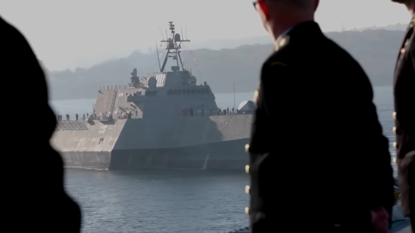 A naval ship in the distance, viewed from the perspective of uniformed personnel onshore